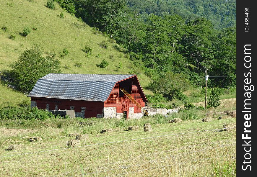 A red barn in a rural area with a hayfield