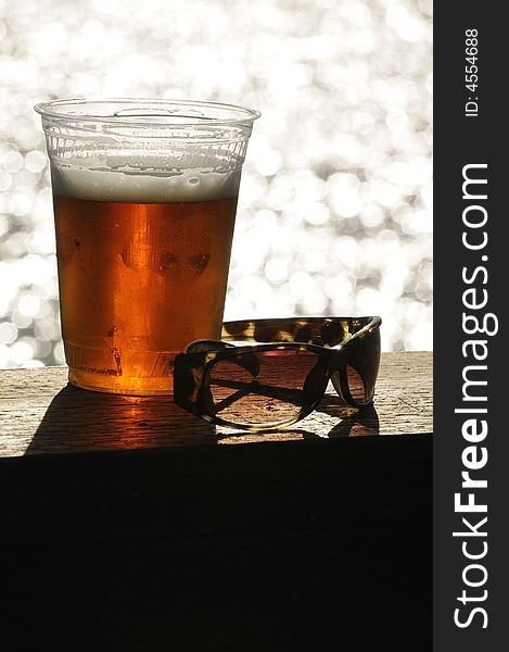 Glass of beer and a pair of sunglassas sitting on a deck handrail overlooking the ocean. Glass of beer and a pair of sunglassas sitting on a deck handrail overlooking the ocean
