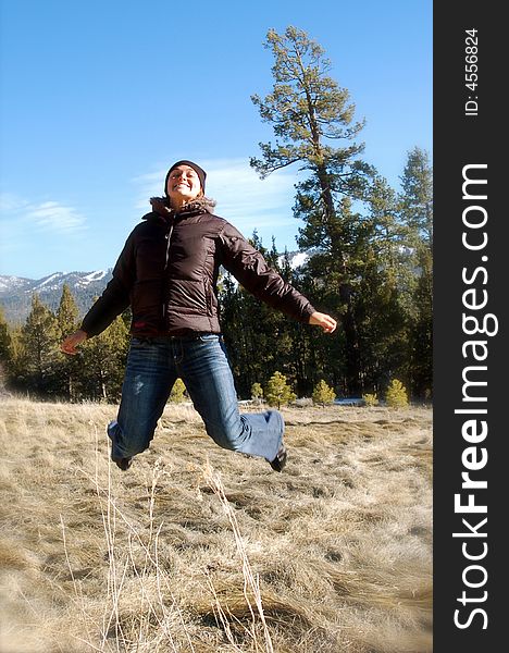 A woman jumps in a field with trees and mountains in the background. A woman jumps in a field with trees and mountains in the background.