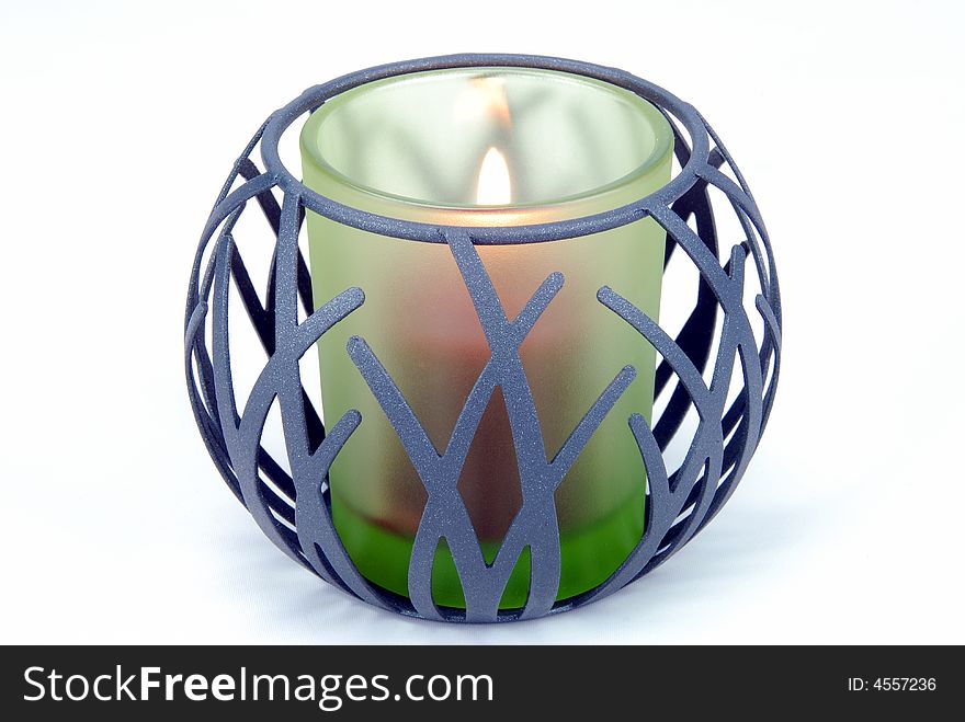 A burning candle in a holder on a white backgroung.