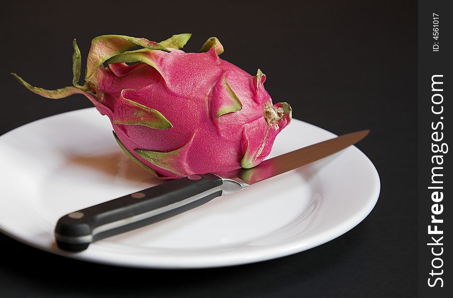 A ripe Dragon Fruit on a plate with a sharp knife, ready for cutting.