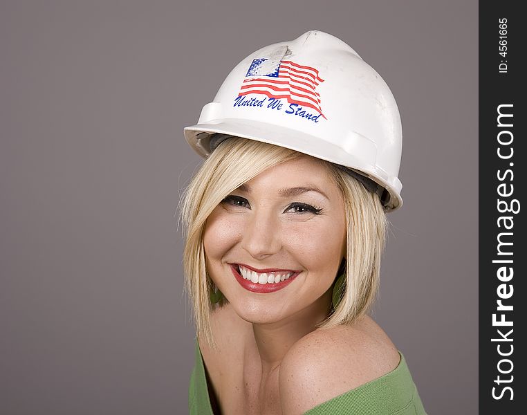 A blonde wearing a construction hard hat and smiling at the camera. A blonde wearing a construction hard hat and smiling at the camera