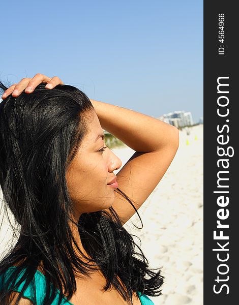 Woman at the beach with her hand on her head.