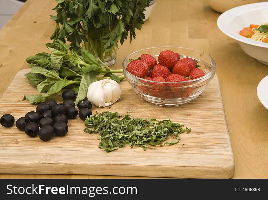 Strawberries inside a bowl, black olives, garlic and basil on top of a wood cutting board. Strawberries inside a bowl, black olives, garlic and basil on top of a wood cutting board.