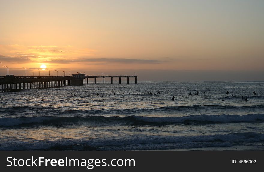 This is a photo of the Ocean Beach Pier in San Diego, California and many surfers waiting for surf as the sun is starting to set. This is a photo of the Ocean Beach Pier in San Diego, California and many surfers waiting for surf as the sun is starting to set.