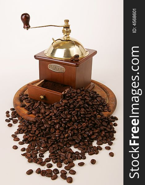 A coffee-mill on a wooden tray and spilt beans. A coffee-mill on a wooden tray and spilt beans