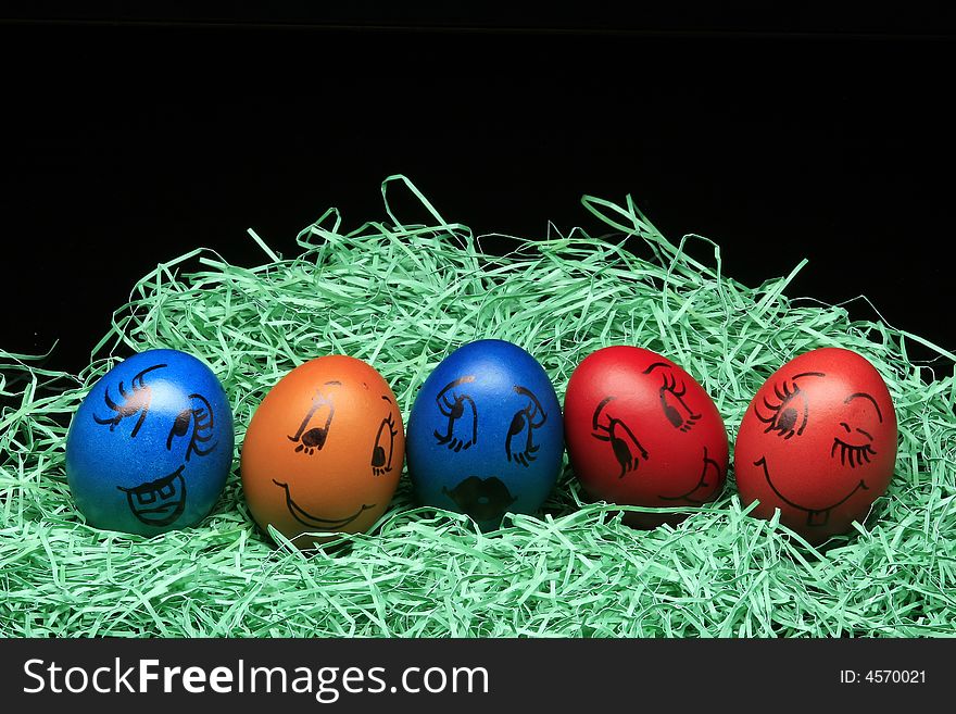 Colored eggs are standing with green on the black background. Colored eggs are standing with green on the black background