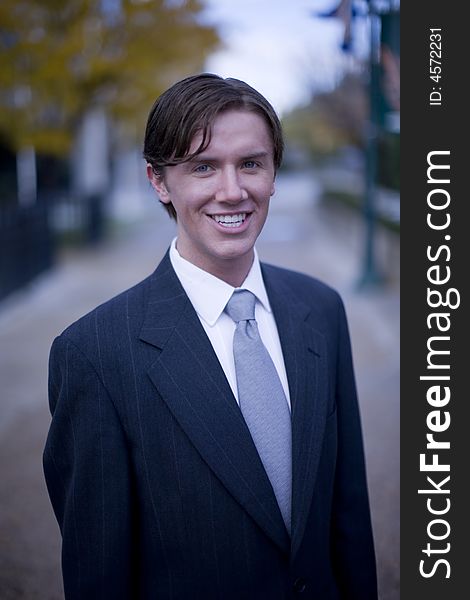 Front view of single white young businessman standing looking at camera with office buildings in background. Front view of single white young businessman standing looking at camera with office buildings in background