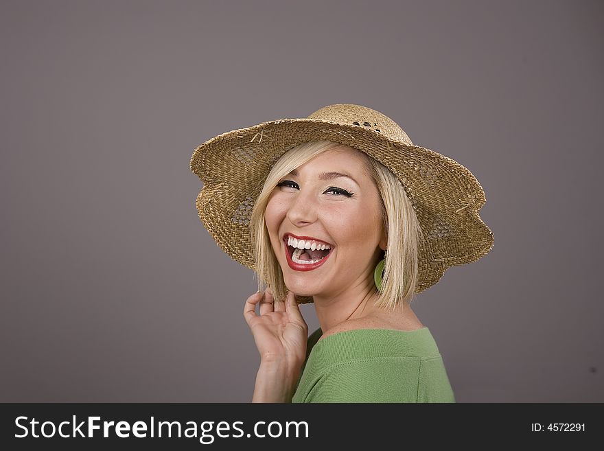 A blonde in a green blouse and a straw hat laughing against a grey background. A blonde in a green blouse and a straw hat laughing against a grey background