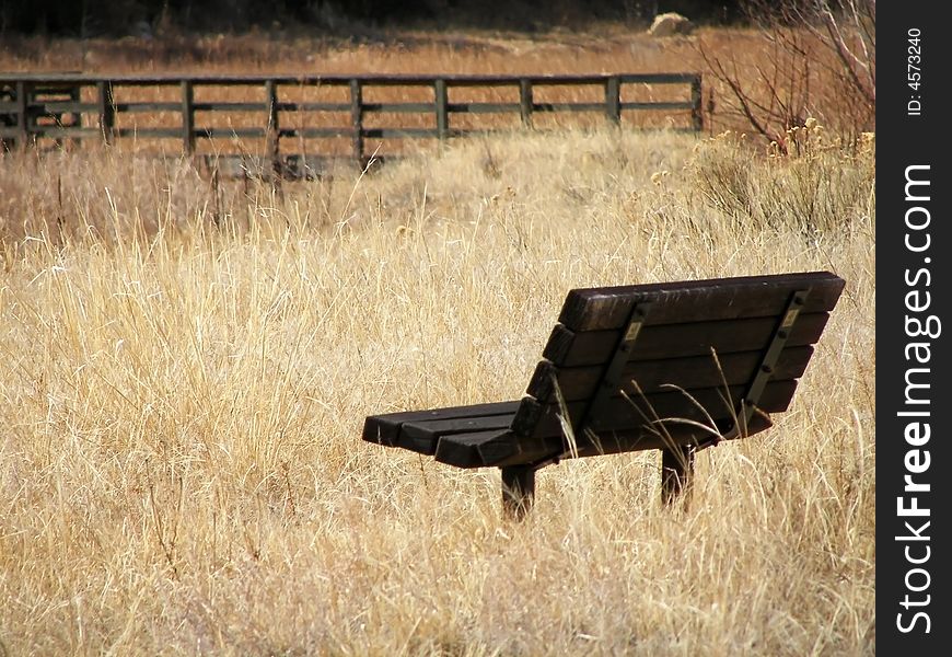A wood bench in a field, on the bank of a river with a bridge in the background. A wood bench in a field, on the bank of a river with a bridge in the background.