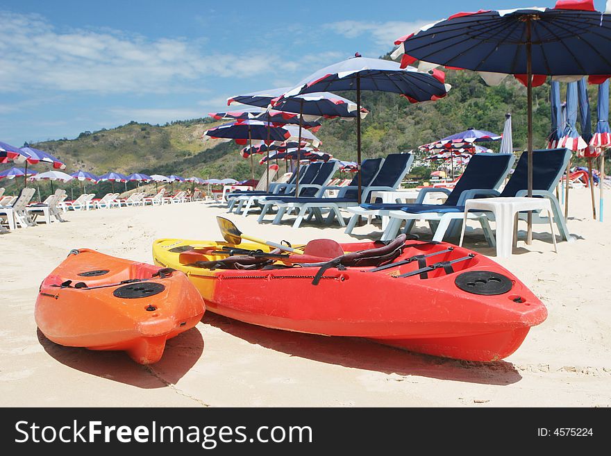 Two sea kayaks on the beach surrounded by beach umbrellas.