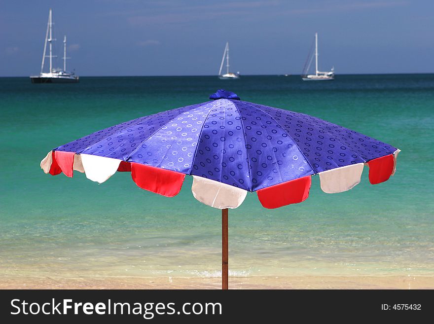 Bright blue and red beach umbrella overlooking the ocean on a summer day.