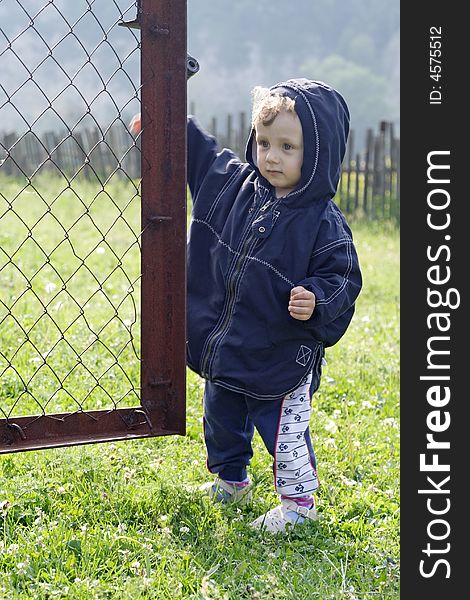 On a background mountains and green grass a little boy opens a metallic gate. On a background mountains and green grass a little boy opens a metallic gate