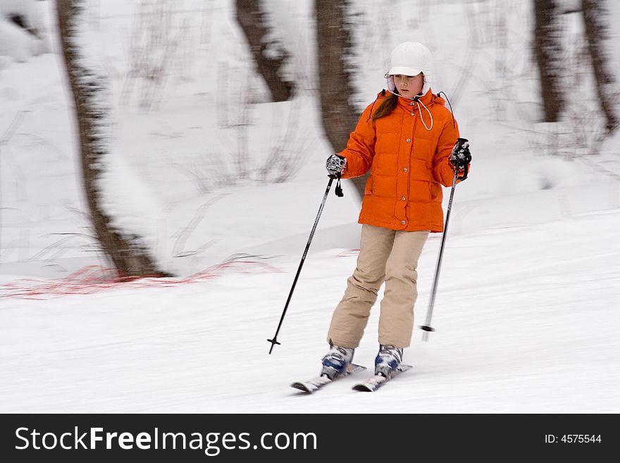 A girl-teenager in an orange jacket and white cap goes for a drive on mountain ski. A girl-teenager in an orange jacket and white cap goes for a drive on mountain ski
