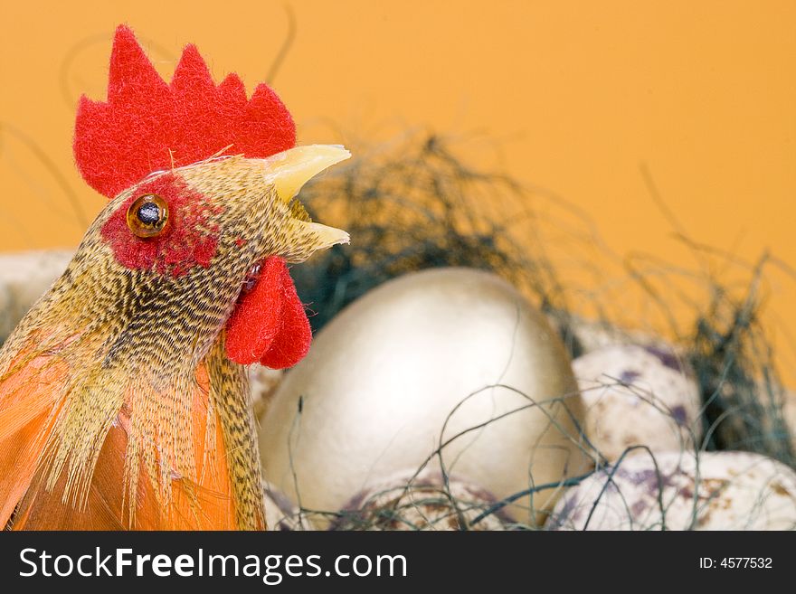 Cock and eggs and gold egg in a nest on a yellow background. Selective focus. Cock and eggs and gold egg in a nest on a yellow background. Selective focus.