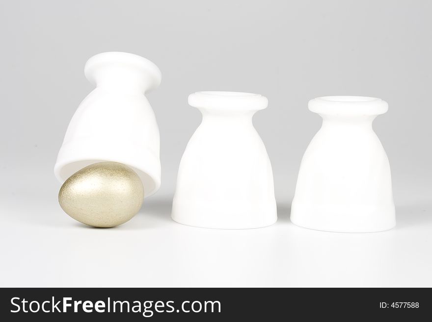 Three eggcups and gold egg on a white background. Concept for Thimblerig.