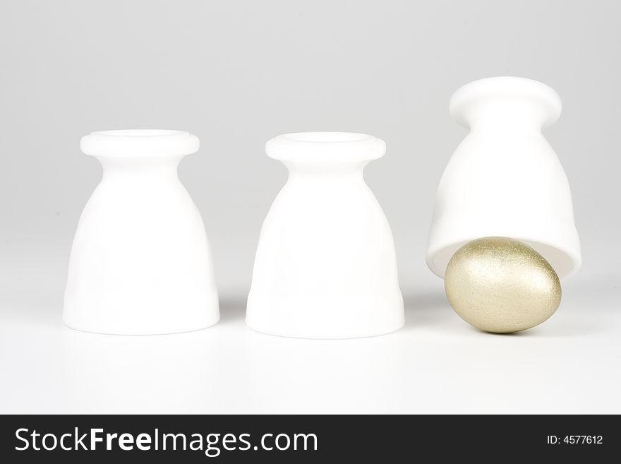 Three eggcups and gold egg on a white background. Concept for Thimblerig.