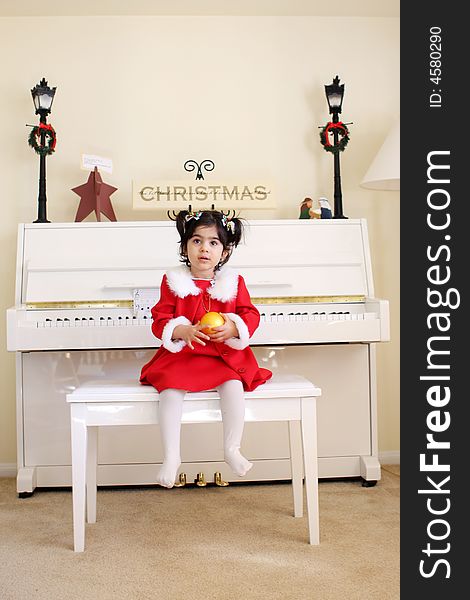 A child playing a white piano wearing a red dress