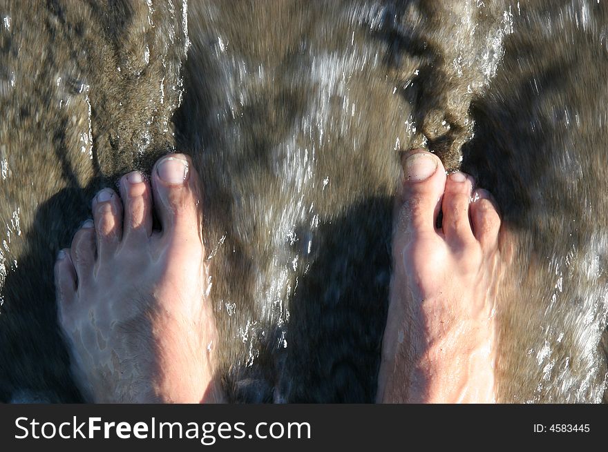 A pair of feet are touched by the sea. A pair of feet are touched by the sea