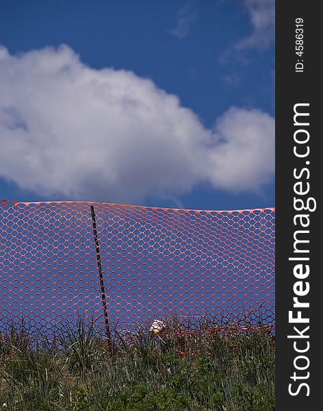 Orange construction fence on grassy hill with blue sky and puffy white clouds. Orange construction fence on grassy hill with blue sky and puffy white clouds