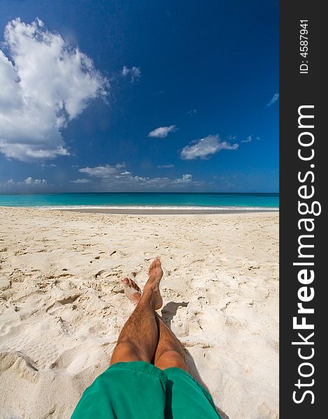 Lone man sitting on white sand beach by turquoise waters on tropical island. Lone man sitting on white sand beach by turquoise waters on tropical island