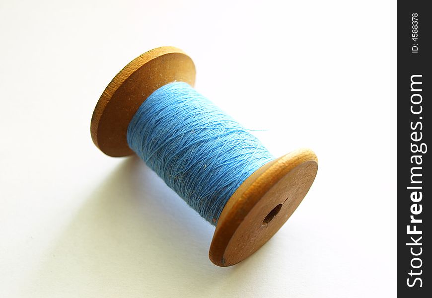 Photo of wooden bobbin with blue, cotton thread. Photo of wooden bobbin with blue, cotton thread