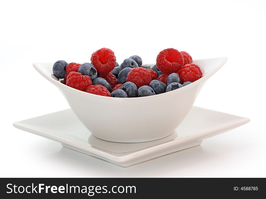 Raspberries and blueberries in bowl isolated on white background