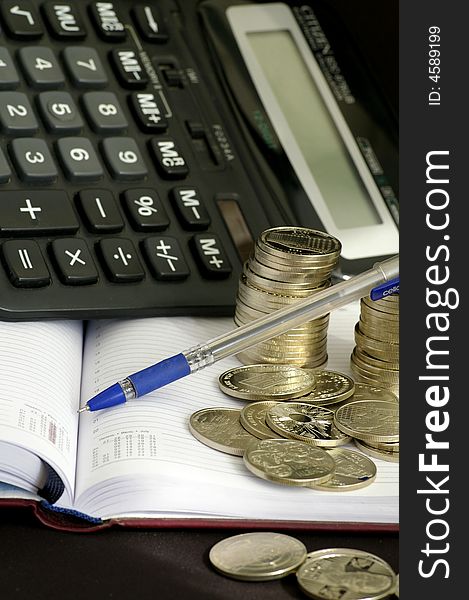 On the black background lies the notebook and many silver coins, and so there is a calculator. On the black background lies the notebook and many silver coins, and so there is a calculator.