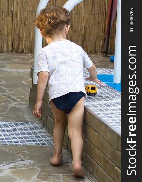 A curly little boy plays with the toy car of white and yellow color at a pool. A curly little boy plays with the toy car of white and yellow color at a pool