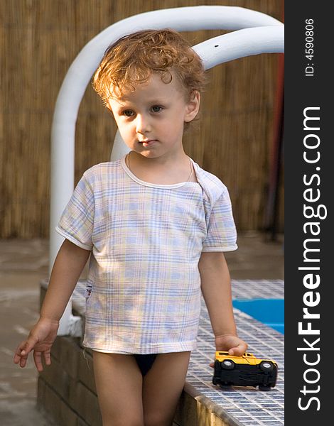 A curly little boy plays with the toy car of white and yellow color at a pool. A curly little boy plays with the toy car of white and yellow color at a pool