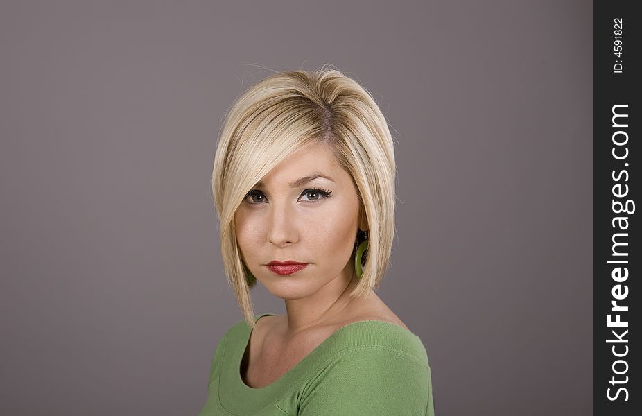 A pretty blonde girl in a green blouse with sad eyes against a grey background. A pretty blonde girl in a green blouse with sad eyes against a grey background