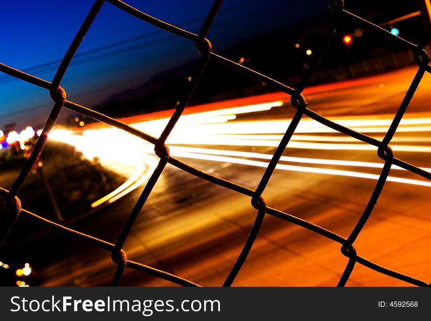 Night time traffic behind a fence on an overpass. Night time traffic behind a fence on an overpass
