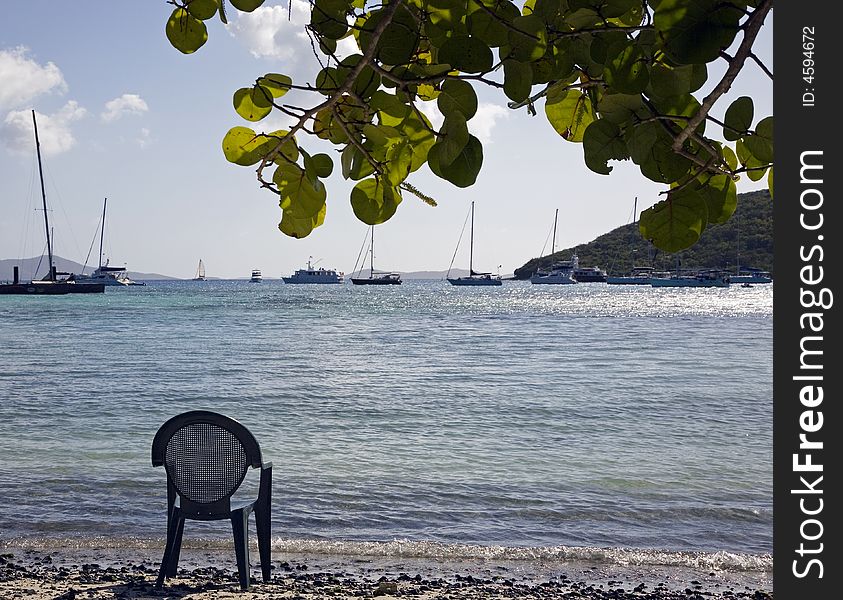Empty chair on a beach with sailboats in the background. Empty chair on a beach with sailboats in the background.