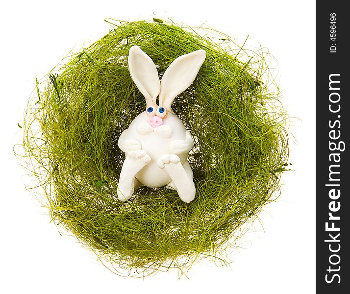 Easter toy white rabbit in a nest from a green grass on a white background. Easter toy white rabbit in a nest from a green grass on a white background