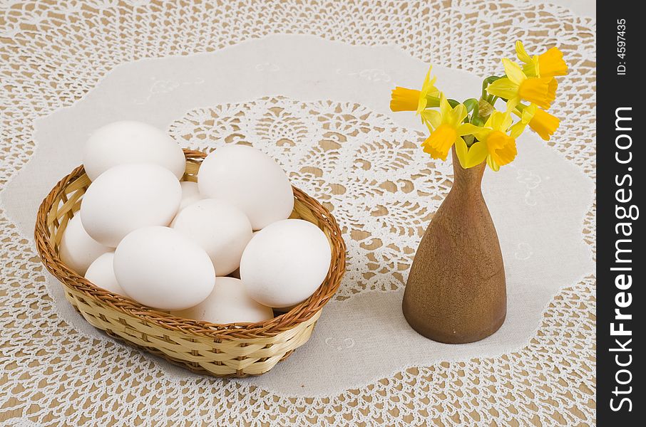 A basket of eggs and yellow daffodils in a vase. A basket of eggs and yellow daffodils in a vase