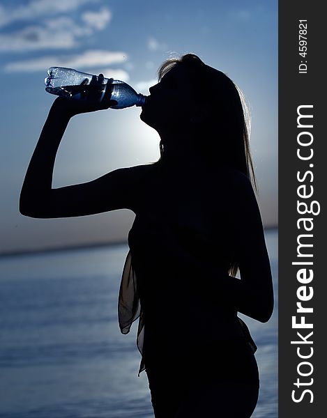 Silhouette of girl drink water on water/sky background. Silhouette of girl drink water on water/sky background