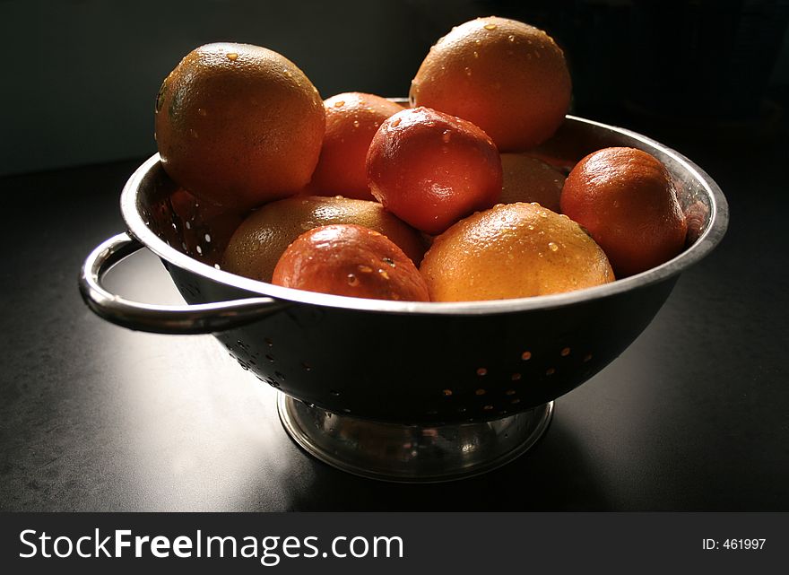 Bunch of citrus in a colander in window light. Bunch of citrus in a colander in window light