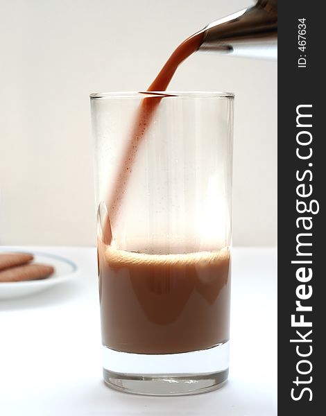 Fresh hot coffee being poured into a glass with some biscuits in the background. Fresh hot coffee being poured into a glass with some biscuits in the background.