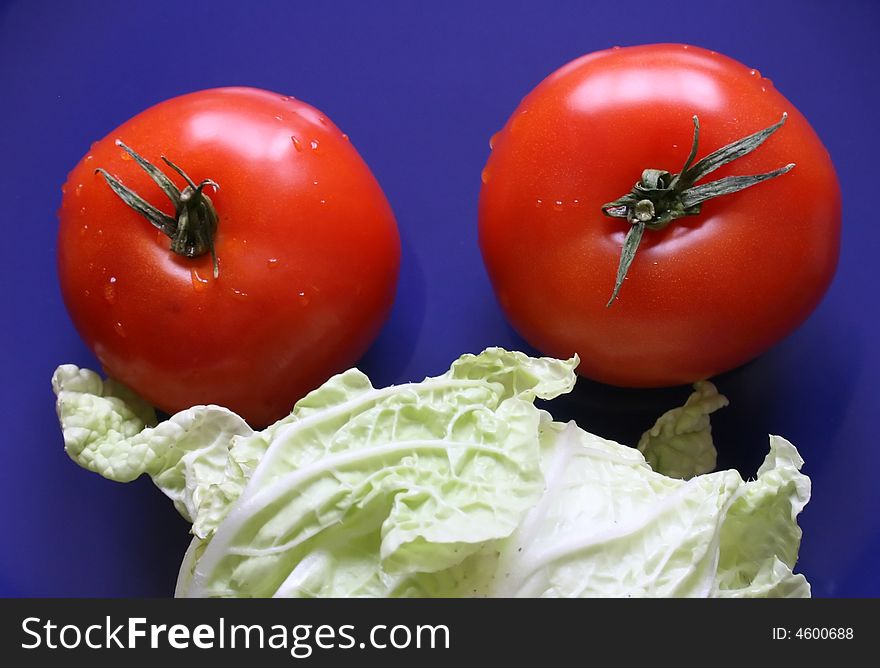 Two red tomatoes and leaf of salad lay on a dark blue dish. Two red tomatoes and leaf of salad lay on a dark blue dish.