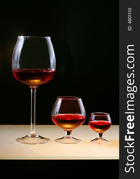 Three glasses of red wine or cognac on lighting bar and on black background.