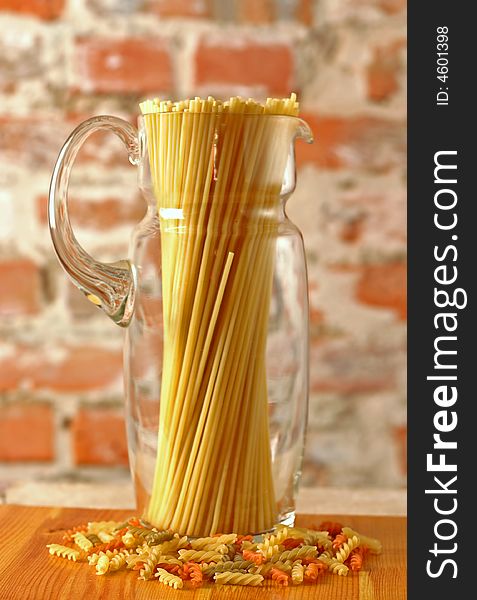 Macaroni in glass jug on brick wall background. Macaroni in glass jug on brick wall background