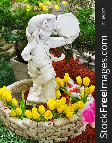 Statue of a boy with tambourine in flowerbasket with tulips in a park. Statue of a boy with tambourine in flowerbasket with tulips in a park