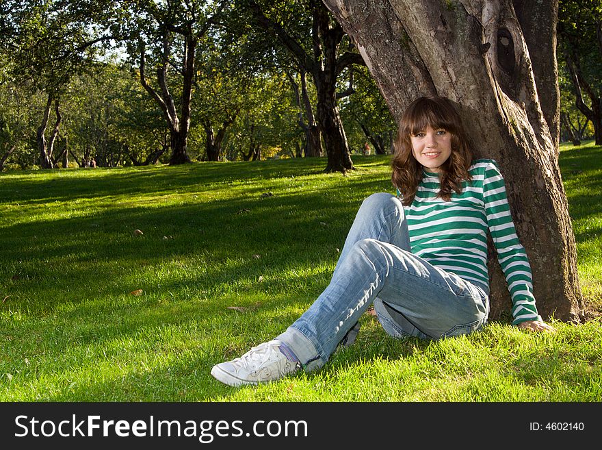 Young beautiful woman sitting at grass near tree and smiling. Young beautiful woman sitting at grass near tree and smiling