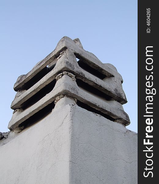 A stone chimney in the top of a building, whit a blue sky behind