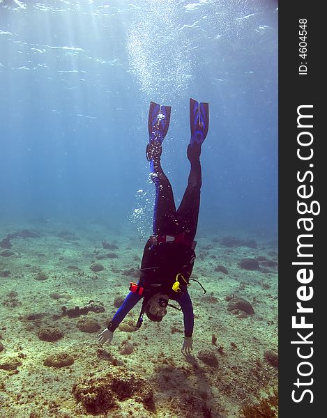 Male scuba diver doing handstand on ocean bottom in clear blue water of caribbean sea