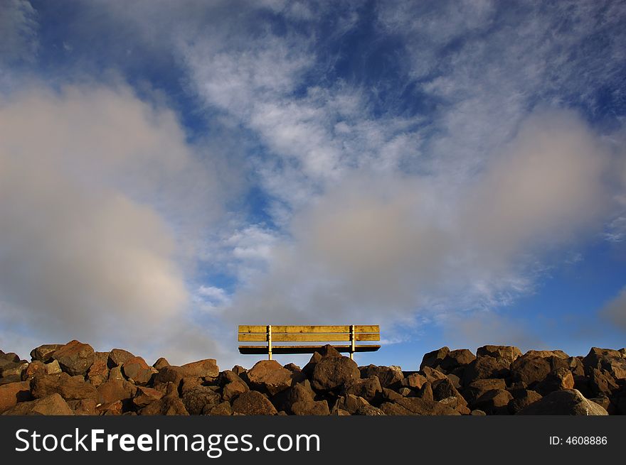 An empty park bench set against dramatic clouds. An empty park bench set against dramatic clouds