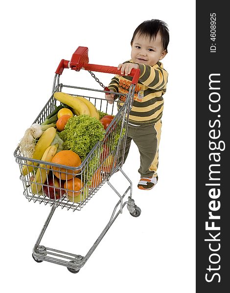 Baby pushes a shopping cart with fruits and vegetables before a white background. Baby pushes a shopping cart with fruits and vegetables before a white background