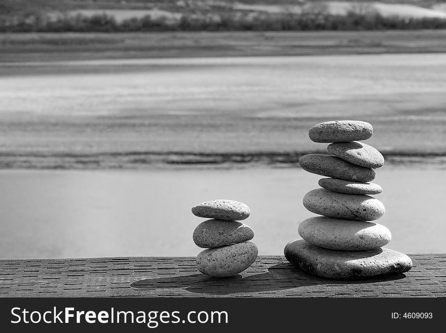 Two stacks of rounded river sones sit on weathered wood in front of a soothing natural background. Two stacks of rounded river sones sit on weathered wood in front of a soothing natural background.
