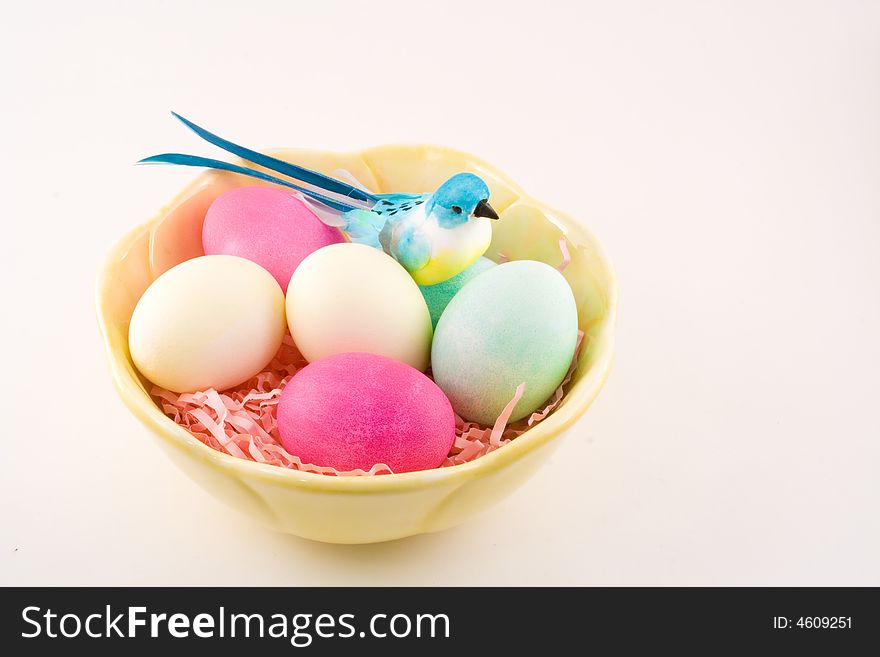 Six colored Easter eggs sit in a pretty yellow bowl with a decorative blue bird perched to one side. Six colored Easter eggs sit in a pretty yellow bowl with a decorative blue bird perched to one side.