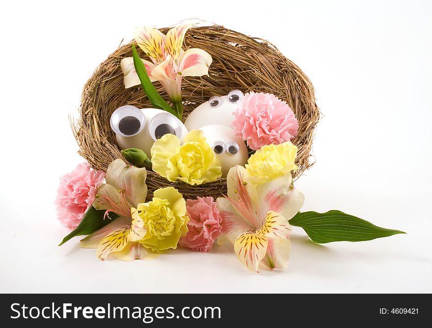 Three googly eyed eggs sit in a birds nest and peep out from among spring colored flowers. Three googly eyed eggs sit in a birds nest and peep out from among spring colored flowers.